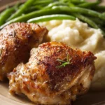 When Weeknight Cravings Hit: Roasted Chicken Thighs with Garlic Mashed Potatoes and Steamed Green Beans 3 Close-up of a chicken thigh dinner with creamy sauce and sides on a white plate.