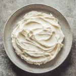 Close-up of a carrot cake slice with cream cheese frosting on a minimal background.